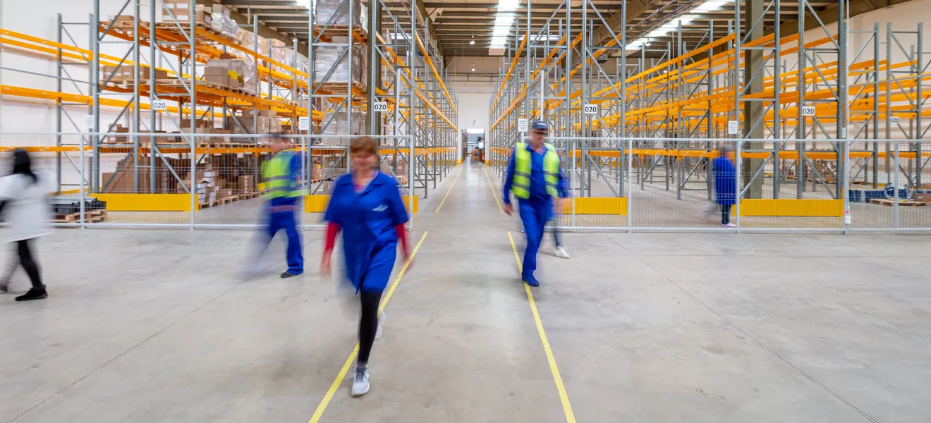 People walking down a wide racked aisle in a distribution center