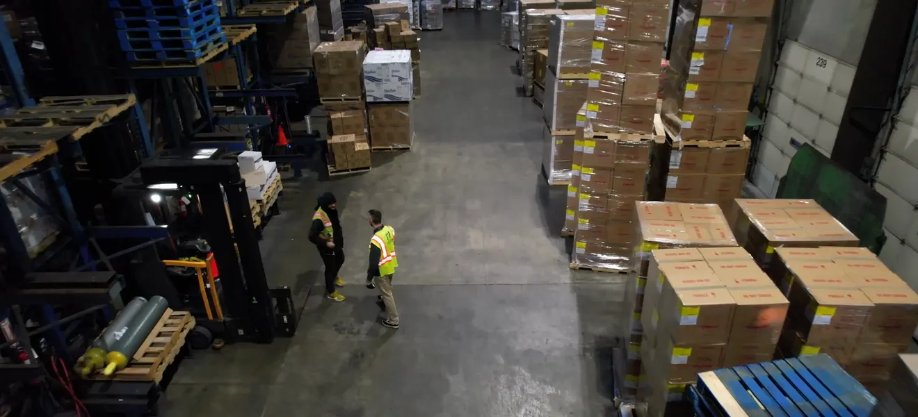 Forklifts and operators among stacked cases on a warehouse floor, seen from above